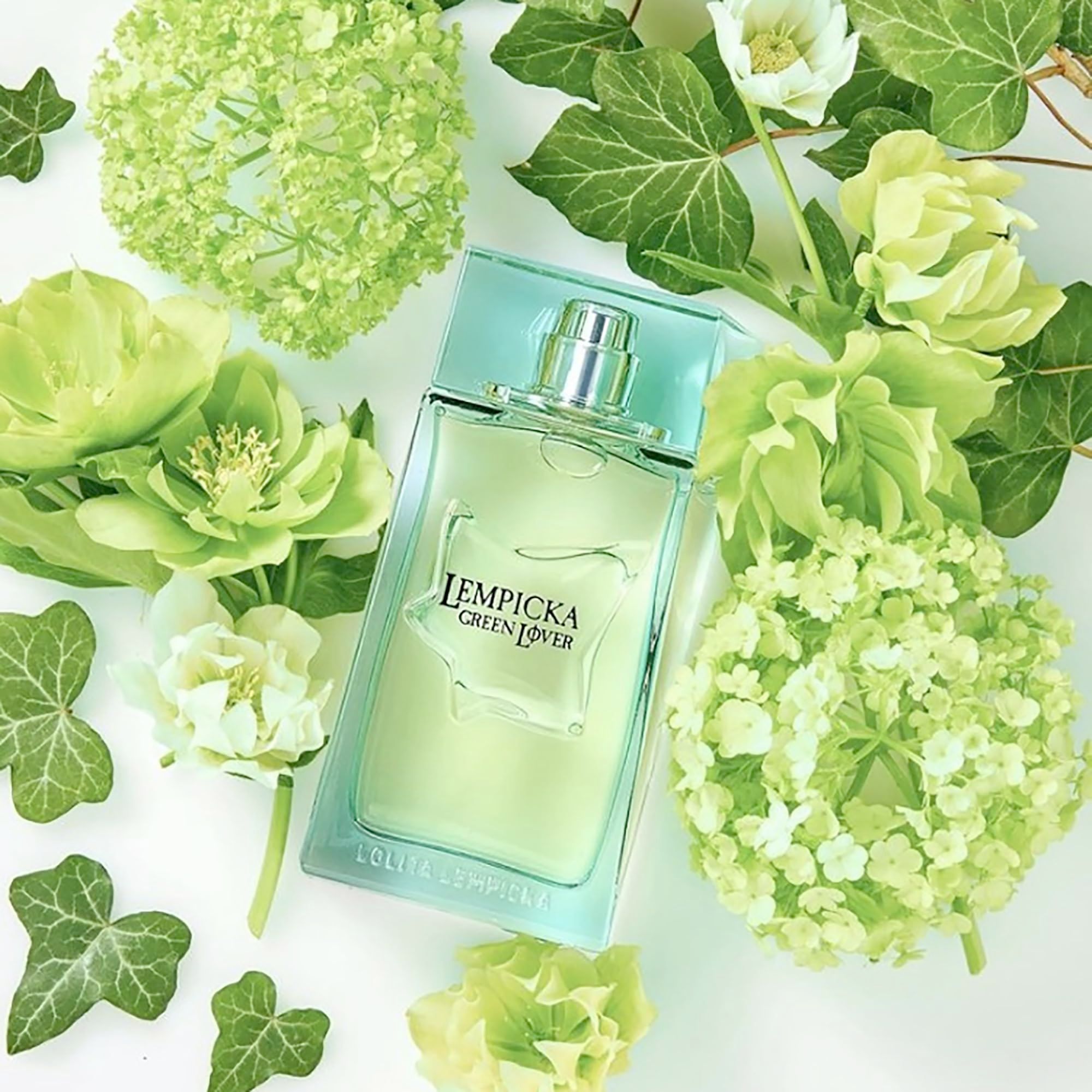 Flacone di profumo verde, circondato da fiori e foglie verdi. Scritta: Lempicka Green Lover.