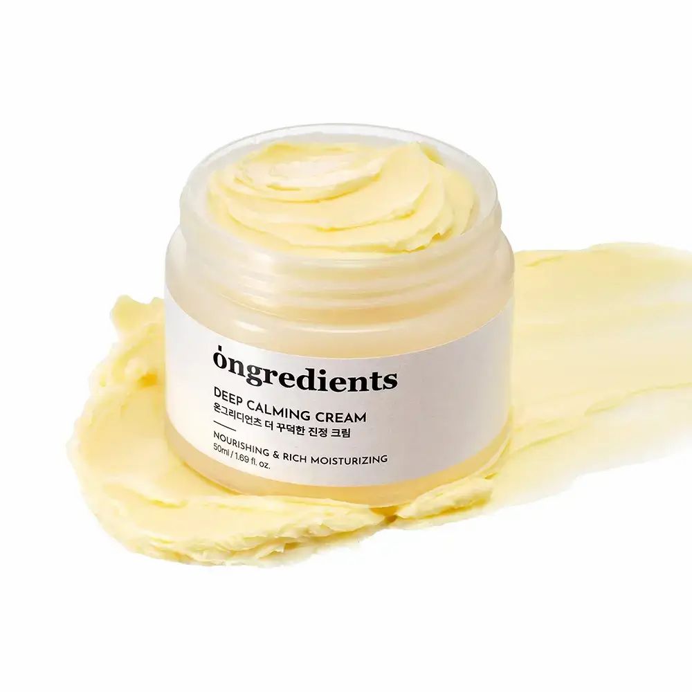 Vasetto di crema aperto con crema gialla. Scritta: "ongredients Deep Calming Cream". Crema su sfondo bianco.