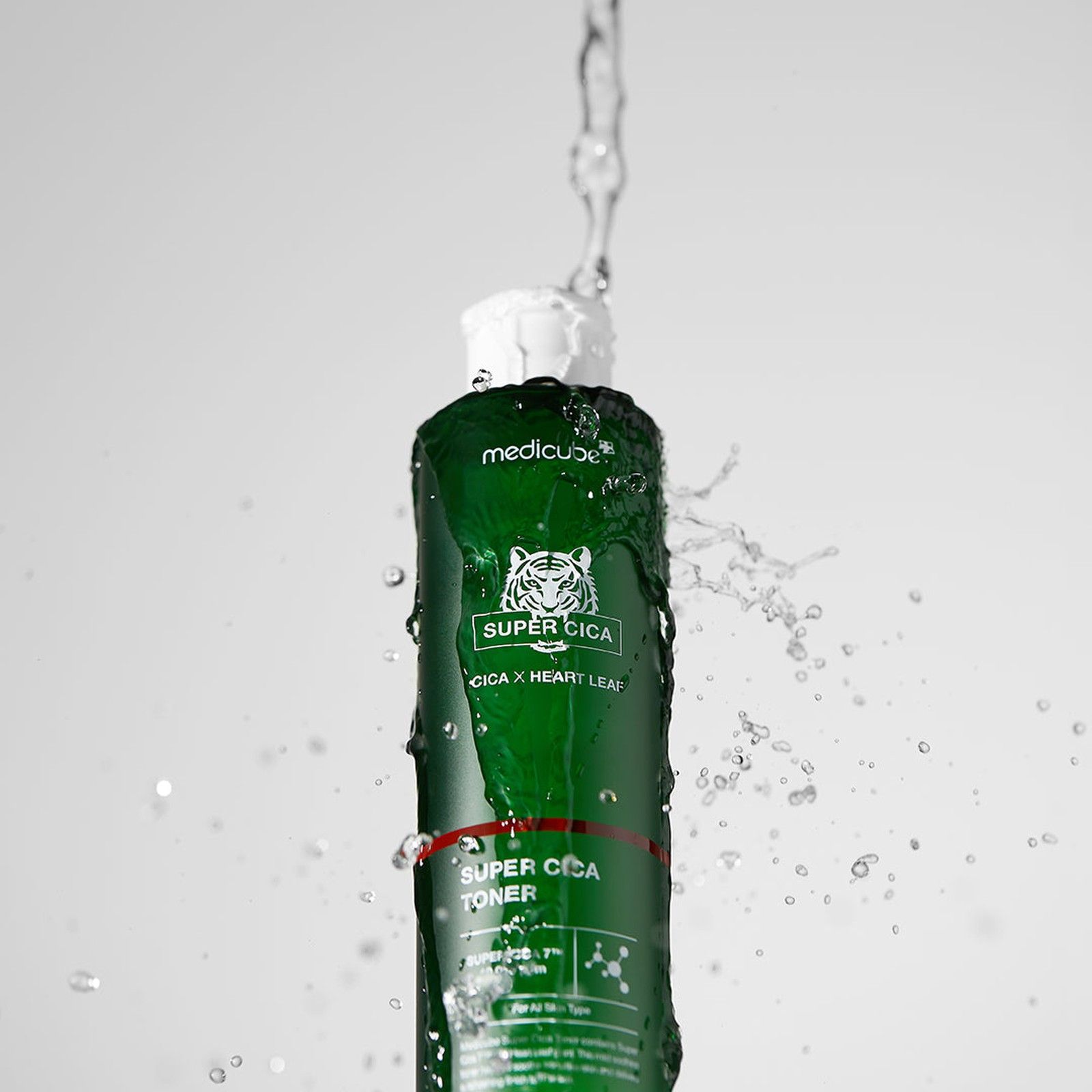 Flacone di MEDICUBE Super Cica Toner circondato da spruzzi d'acqua.