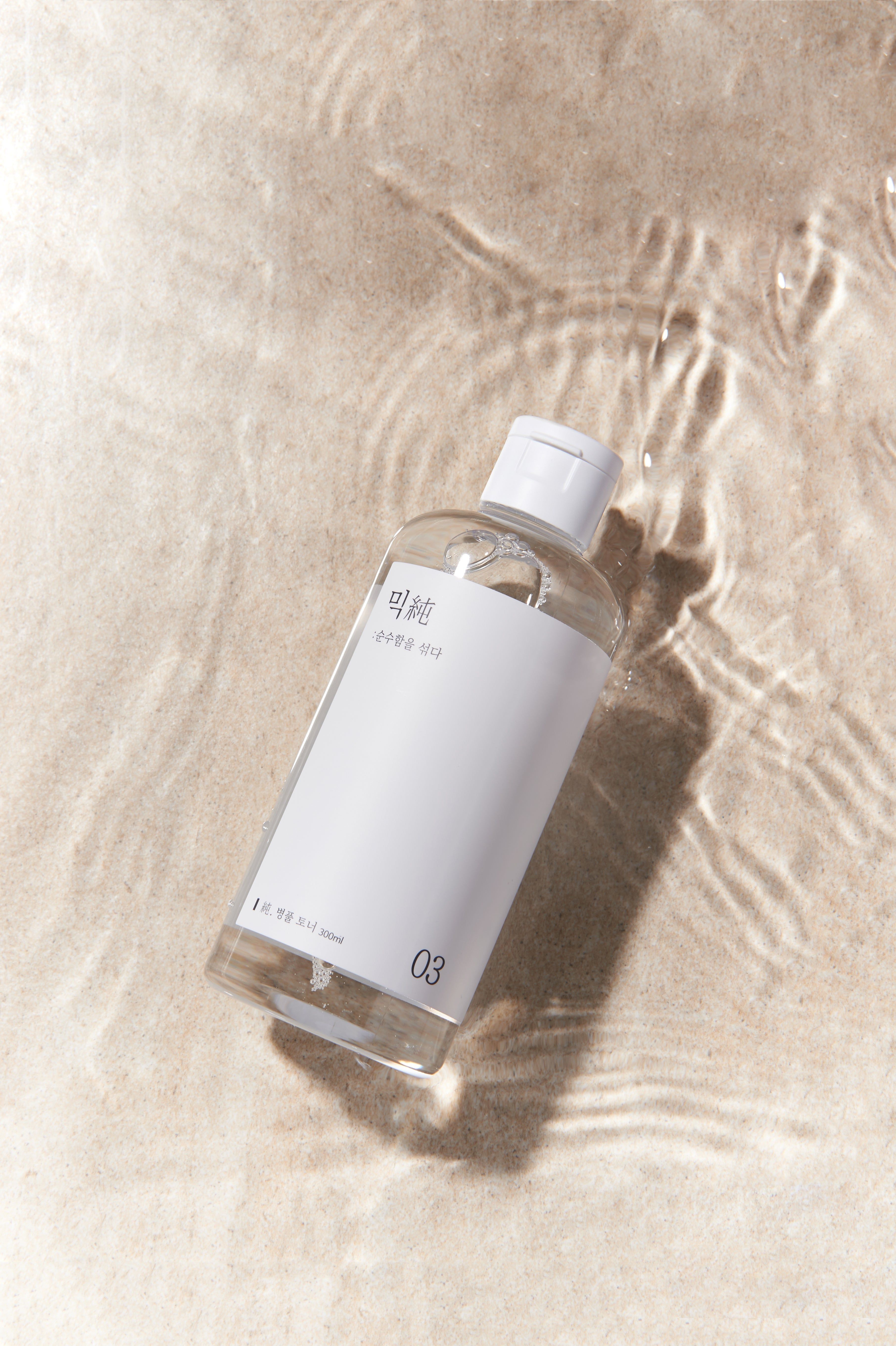 Flacone trasparente con tappo bianco ed etichetta, nell'acqua. Scritta in coreano e il numero 03. Scritta: 200ml.