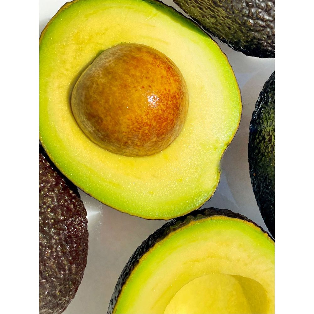 Primo piano di avocado a metà. Polpa verde, nocciolo marrone. Alcuni avocado interi, buccia scura.