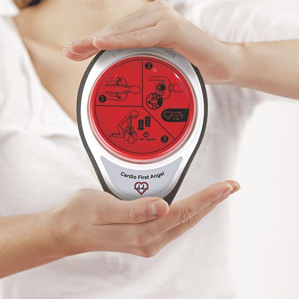 Cardio First Angel tenuto tra le mani. Pulsante rosso con istruzioni, cornice bianca, schiuma grigia. Testo: Cardio First Angel.