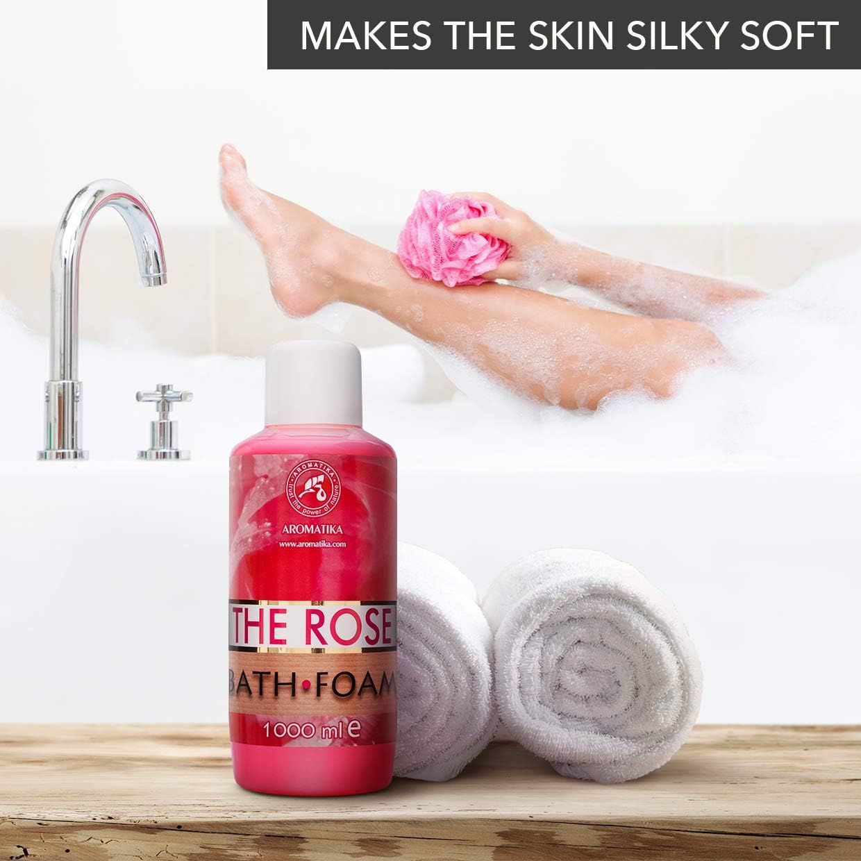 Flacone rosa AROMATIKA THE ROSE BATH FOAM accanto alla vasca. Donna con schiuma e asciugamano. Rubinetto sullo sfondo.