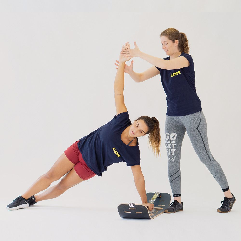 Persona che esegue un plank laterale sul GIBOARD SET - CAESAR JIB, istruttore assiste.