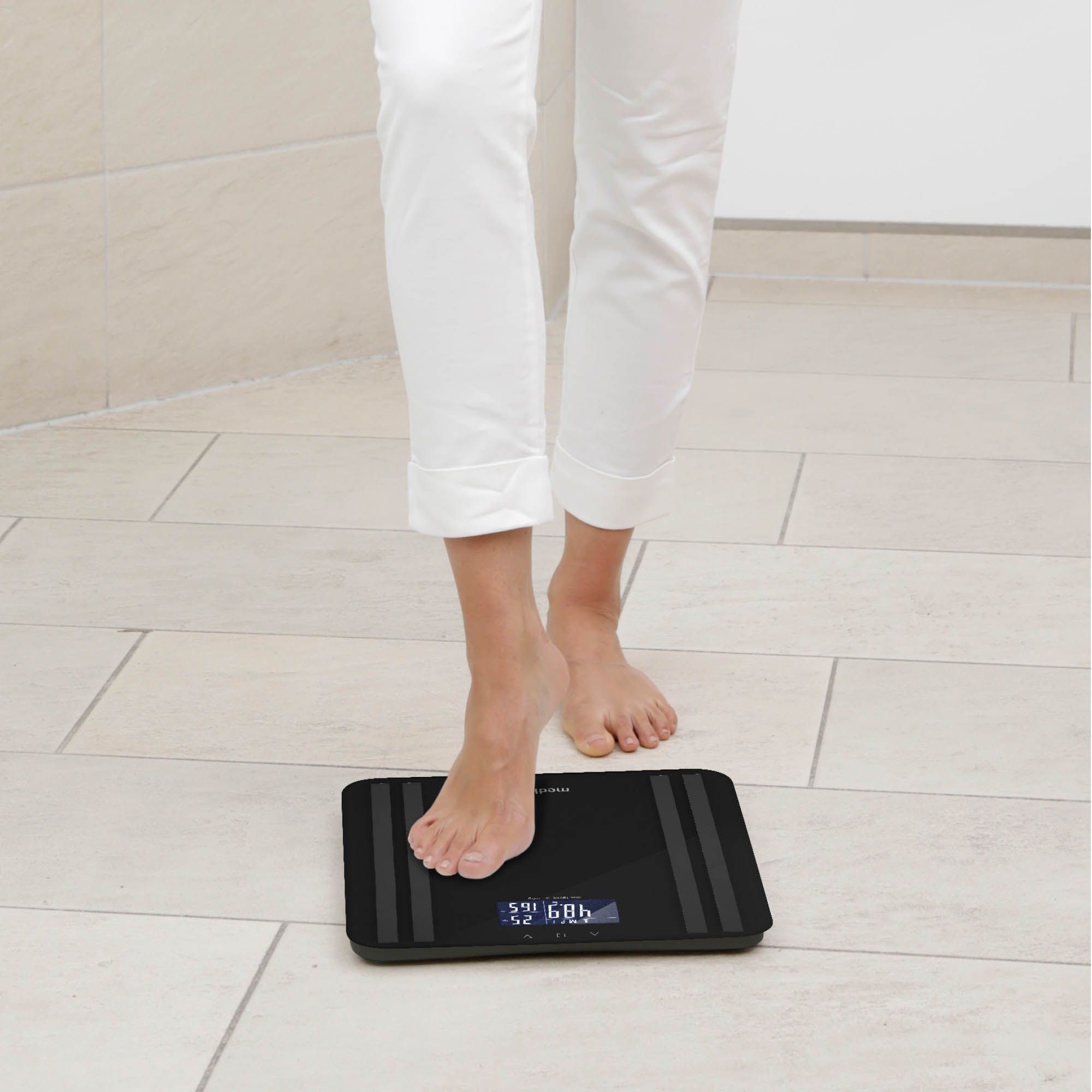 Persona in piedi su una bilancia per analisi corporea nera. Display digitale con dati sul peso. Marchio: medisana.