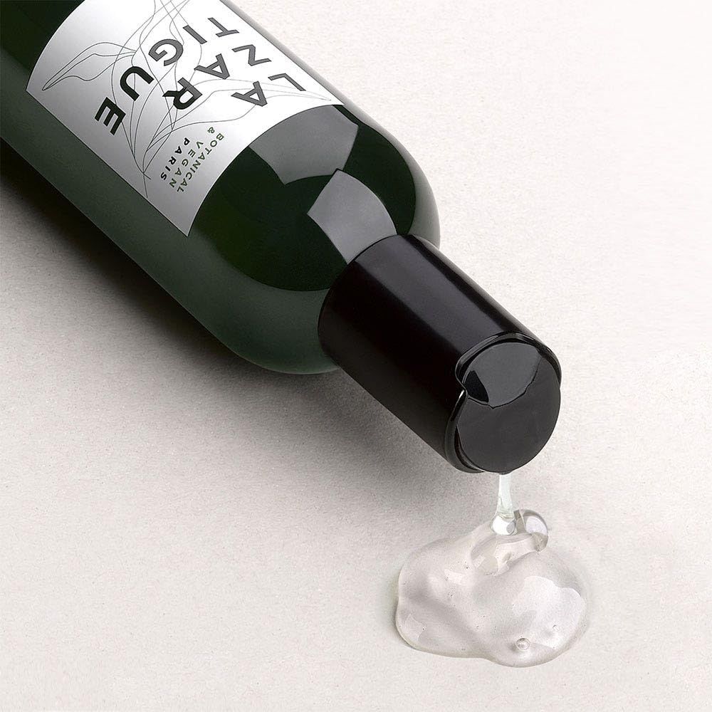 Bottiglia verde con tappo nero, liquido che cola. Scritta: LA ZAR TIGUE.