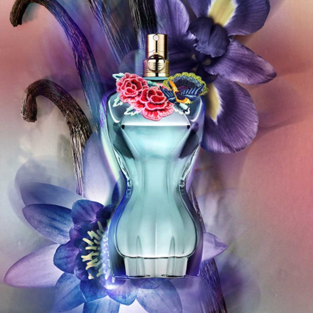 Flacone di profumo blu a forma di corpo femminile, decorato con fiori. Chiusura dorata. Circondato da fiori viola e rosa.