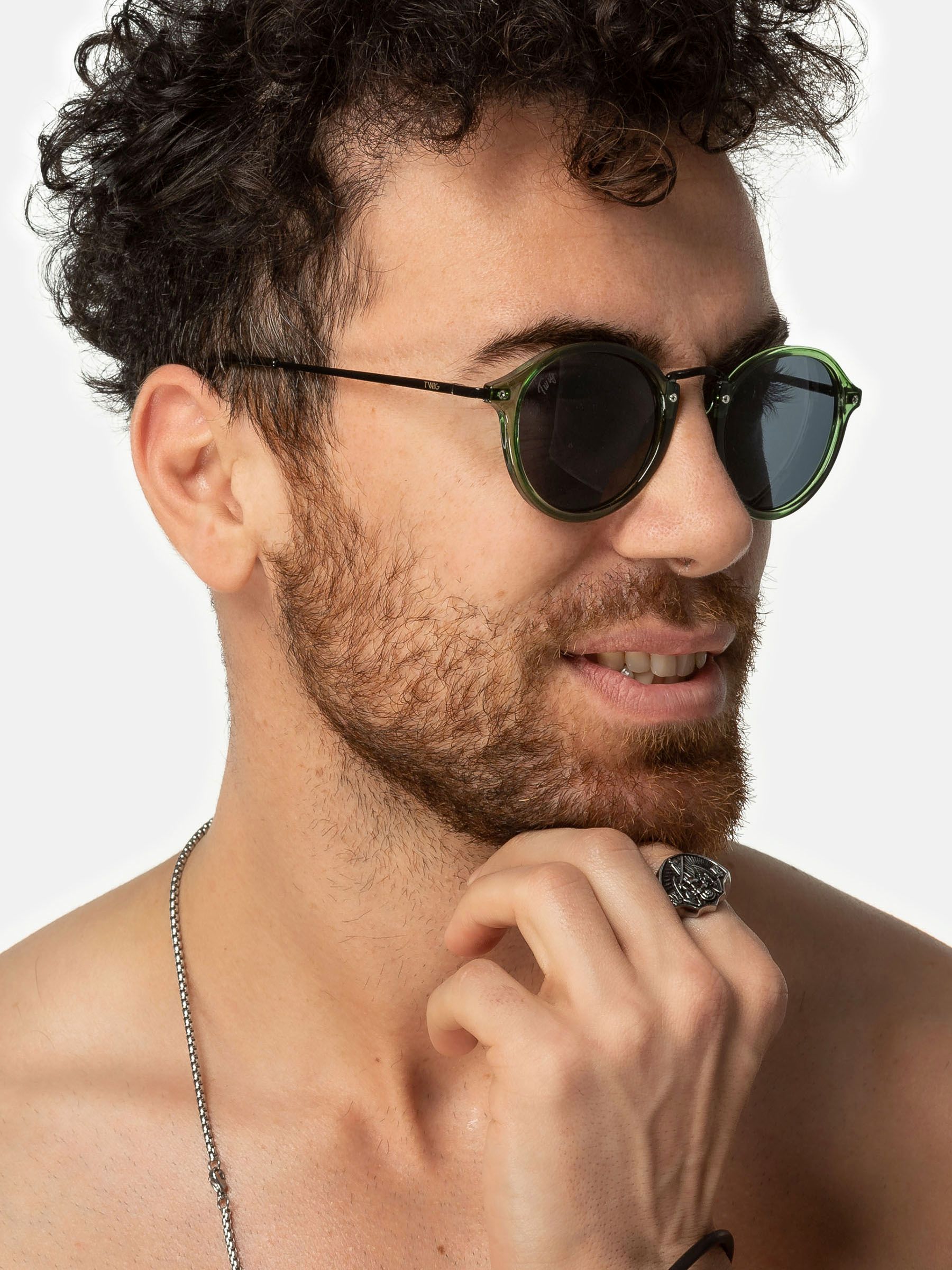 Uomo con occhiali da sole verdi. Lenti rotonde, aste nere. Marchio Twig.