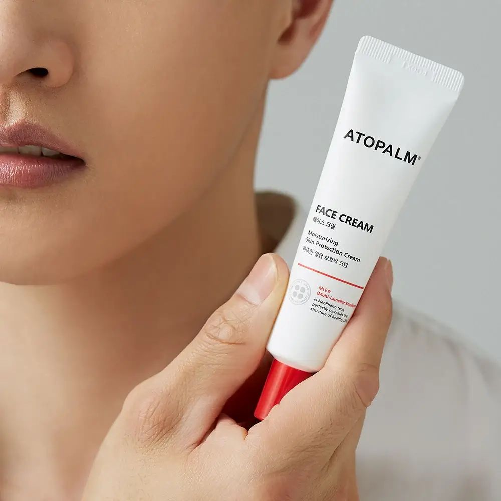 Persona che tiene un tubo con tappo rosso. Scritta ATOPALM FACE CREAM. Informazioni sul prodotto.