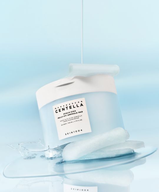 Barattolo blu e bianco SKIN1004. Scritta Hyalu-Cica Jelly Fit Ampoule Pad. Liquido che fuoriesce dal barattolo e sui pad.