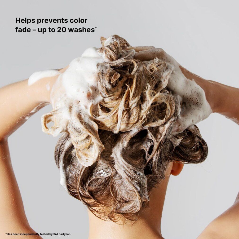 Persona che si lava i capelli con shampoo. Schiuma che copre i capelli. Testo: "Helps prevents color fade - up to 20 washes".