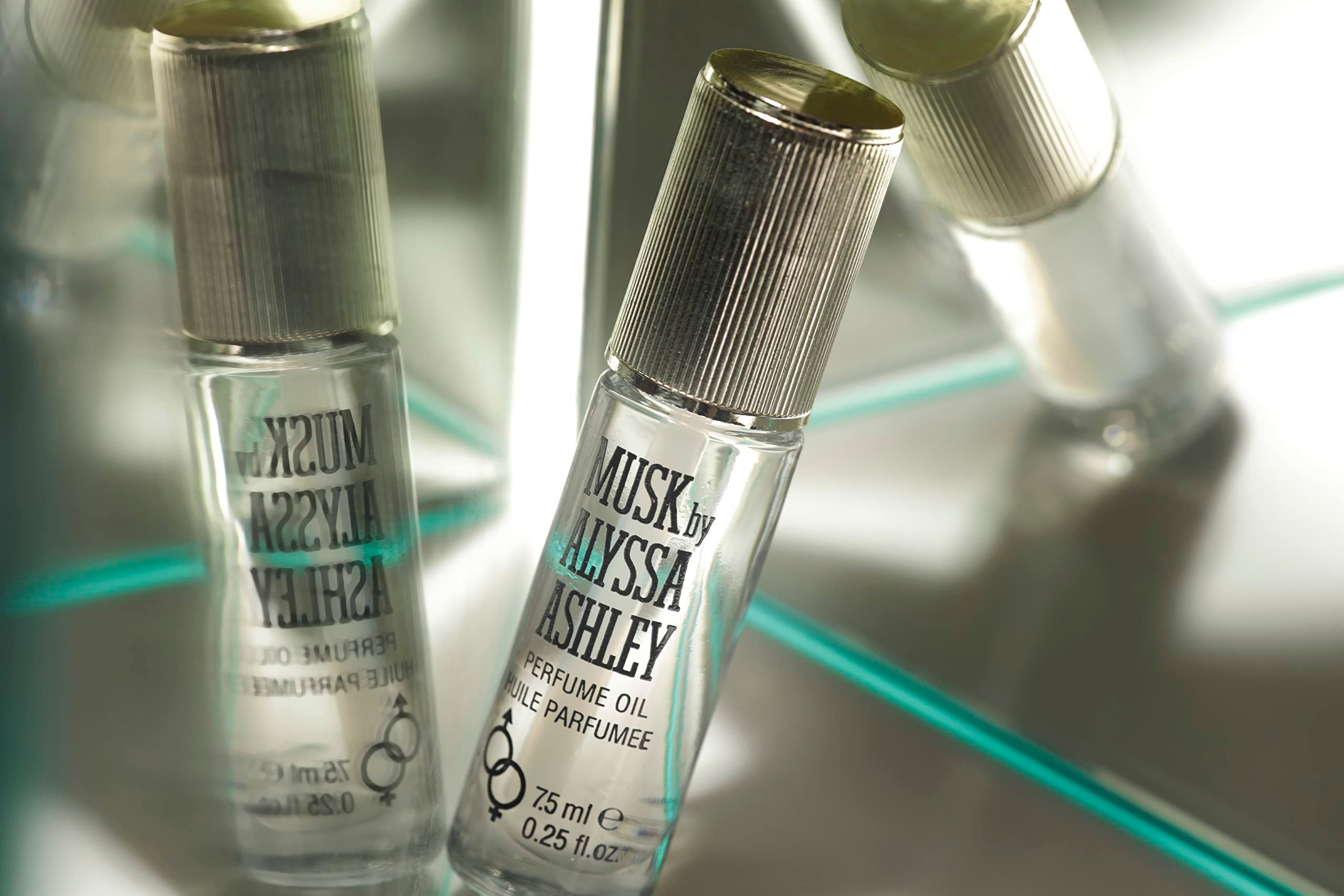 Due flaconi Alyssa Ashley Musk Olio Profumato su superficie specchiata, con tappi dorati.