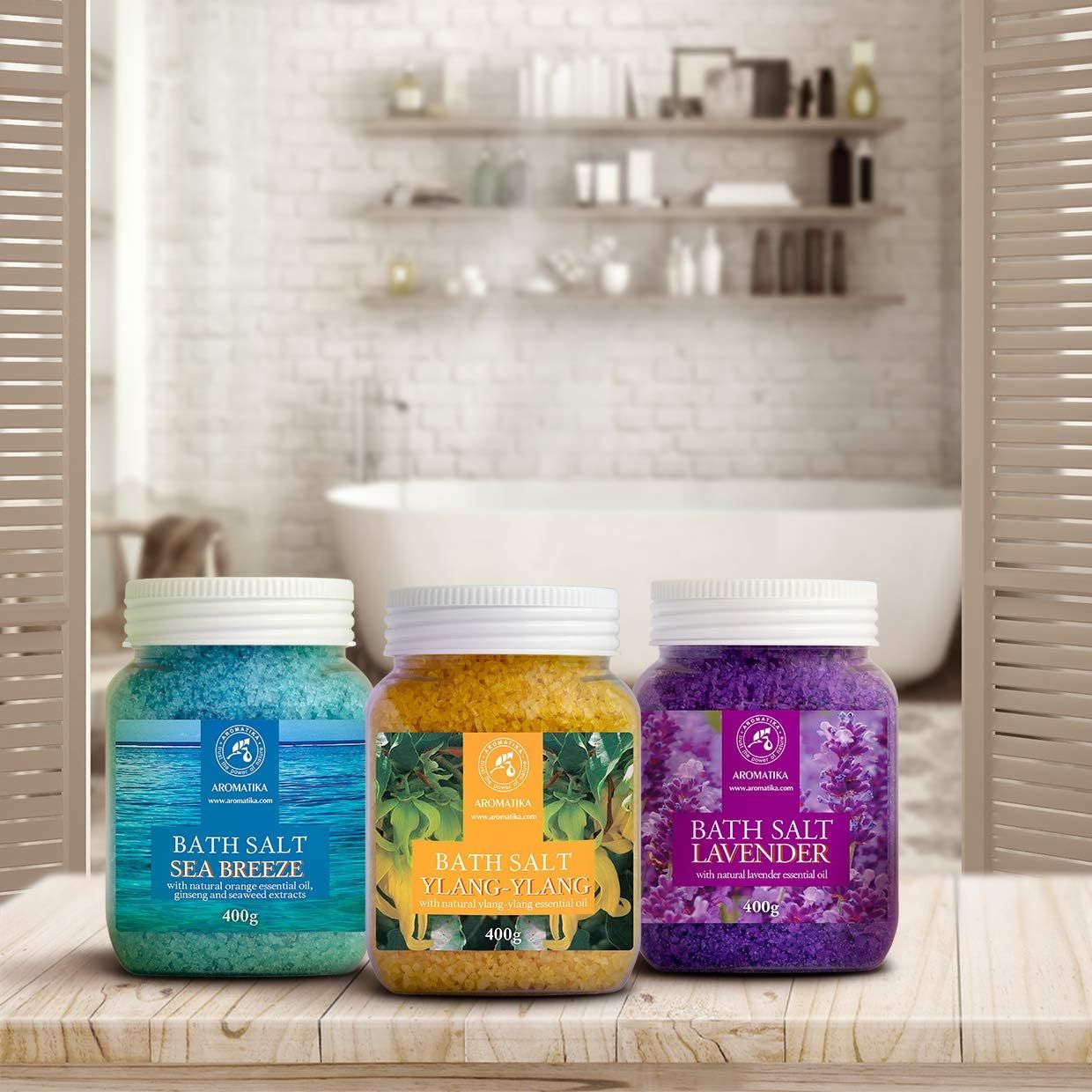 Tre barattoli di sali da bagno su un tavolo. Blu, giallo e viola. Scritte: Sea Breeze, Ylang-Ylang, Lavanda. Sfondo: bagno.