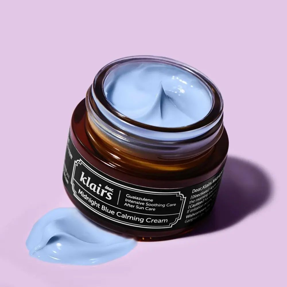 Vasetto di crema aperto, crema blu visibile. Nome del prodotto e marchio sull'etichetta. Macchia di crema accanto.