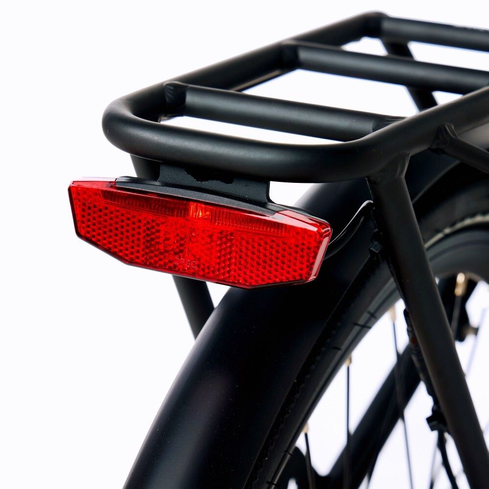 Primo piano della luce posteriore di una bicicletta elettrica. La luce posteriore rossa è fissata a un portapacchi nero.