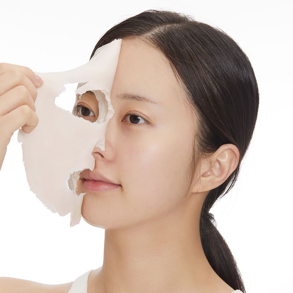 Viso di donna con maschera facciale parzialmente rimossa. Maschera chiara, pelle sottostante visibile.