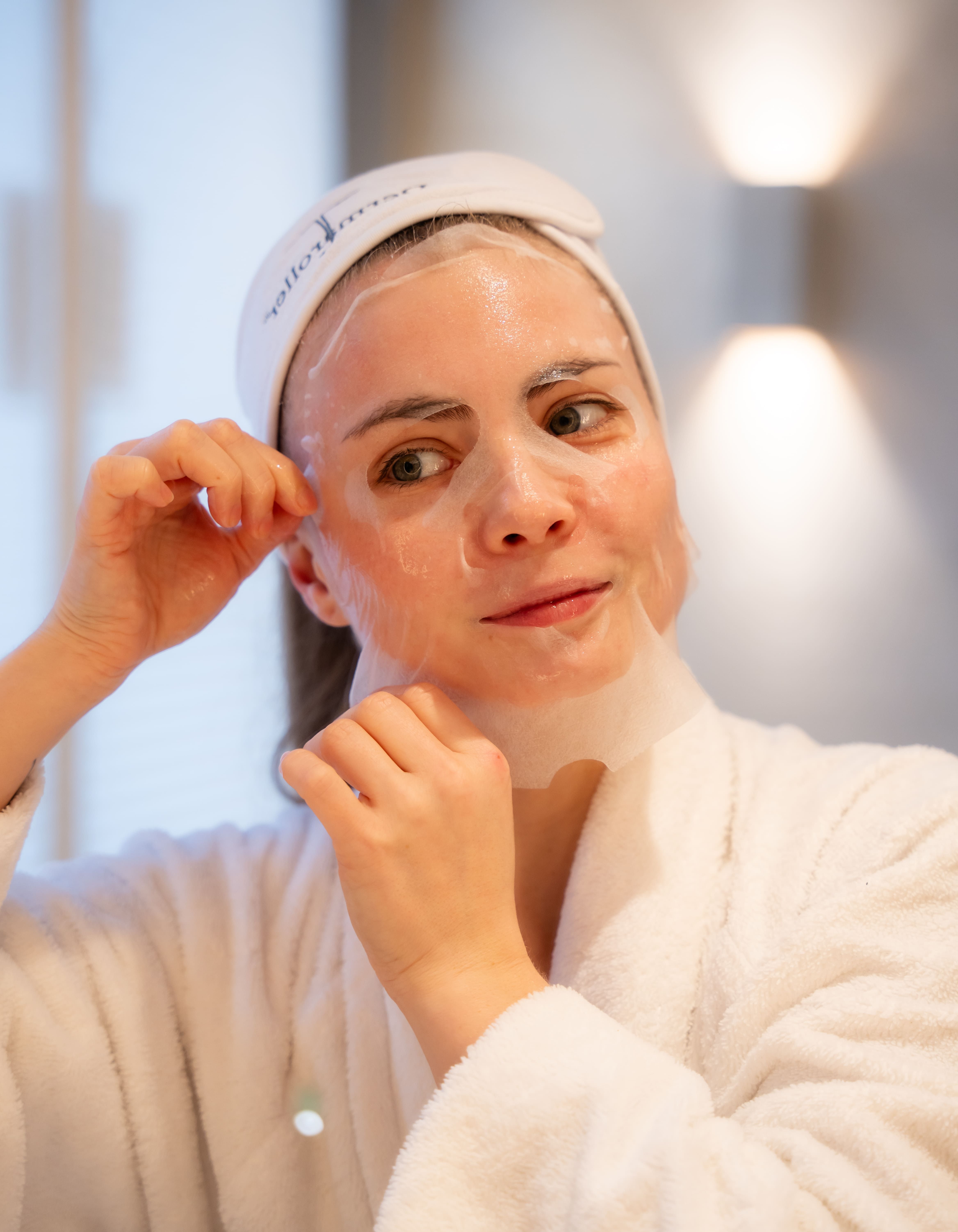 Donna con fascia bianca e accappatoio indossa una maschera in tessuto.