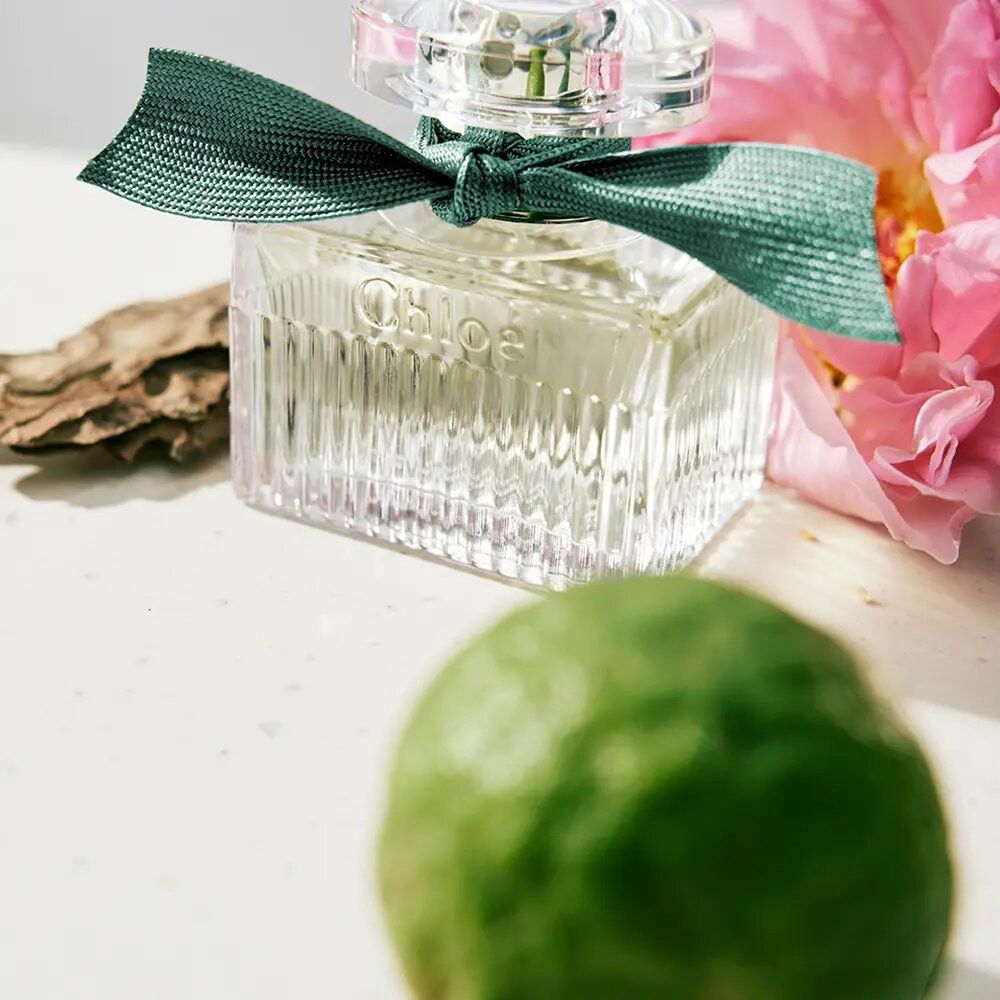 Flacone in vetro con fiocco. Scritta: Chloé. Flacone con nastro verde. Con limone e fiore.