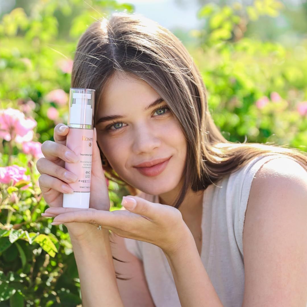 Donna che tiene la crema Rosense Supreme Hydration. Flacone rosa con nome e logo del prodotto. Donna sorridente in un campo di fiori.