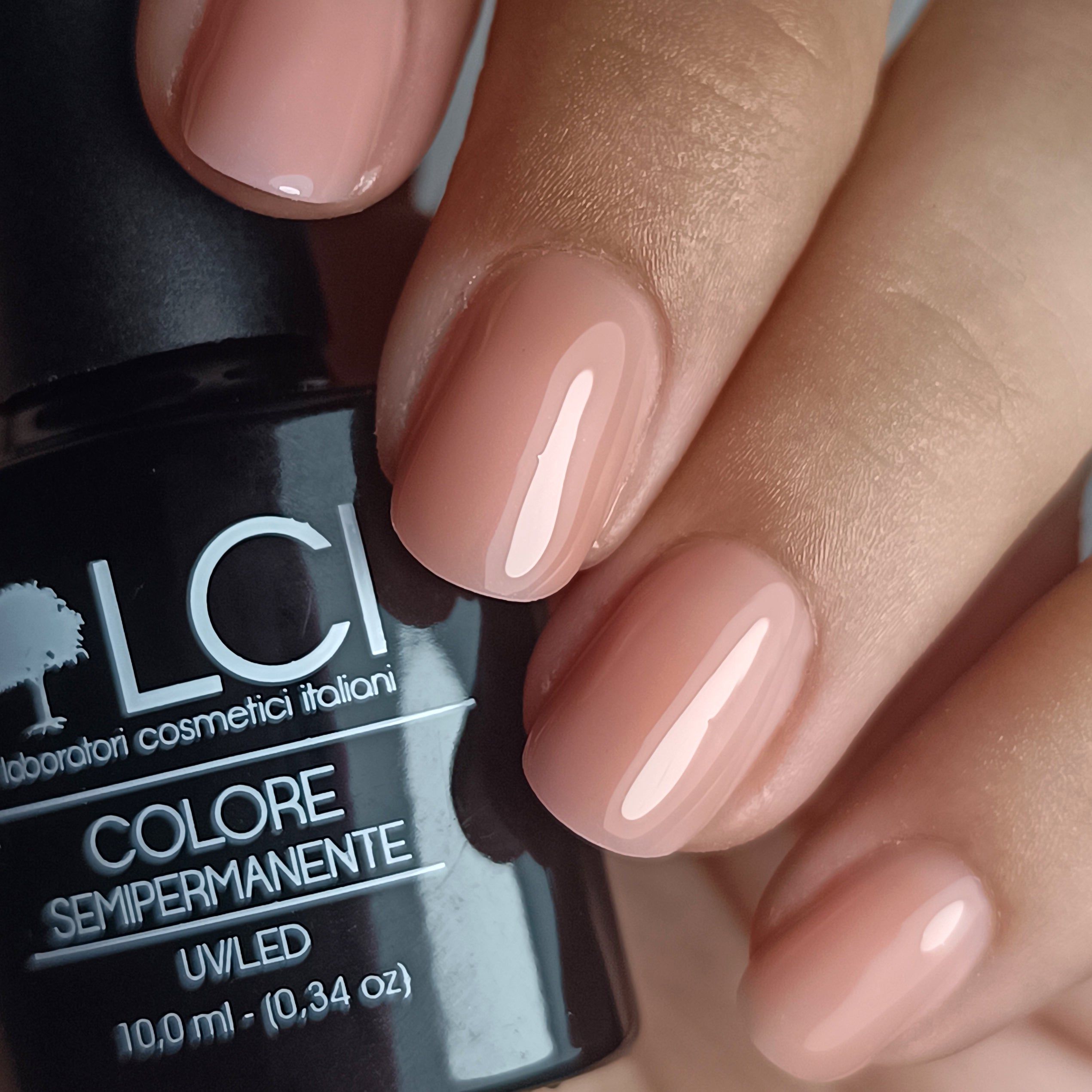 Mano con unghie smaltate rosa. Flacone di smalto con scritta: LCI, Colore Semipermanente, UV/LED, 10,0 ml.