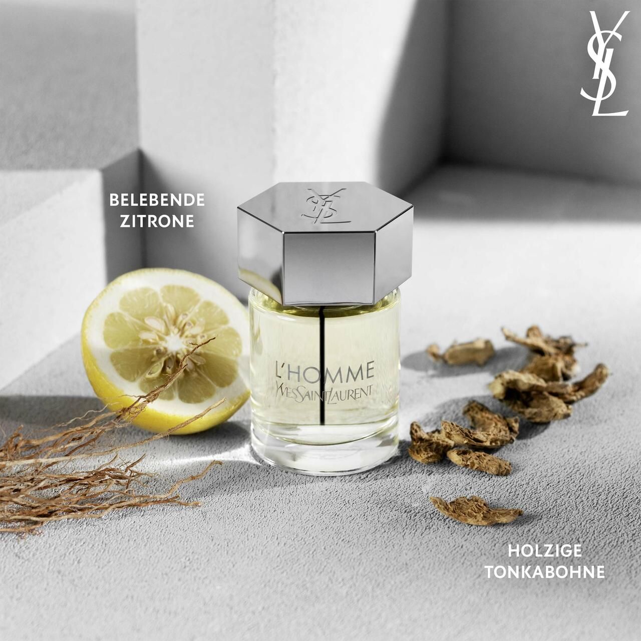 Flacone di profumo con limone e pezzi di legno. Scritta L'HOMME YVES SAINT LAURENT. Tappo argentato. Limone a metà. Fava tonka legnosa.
