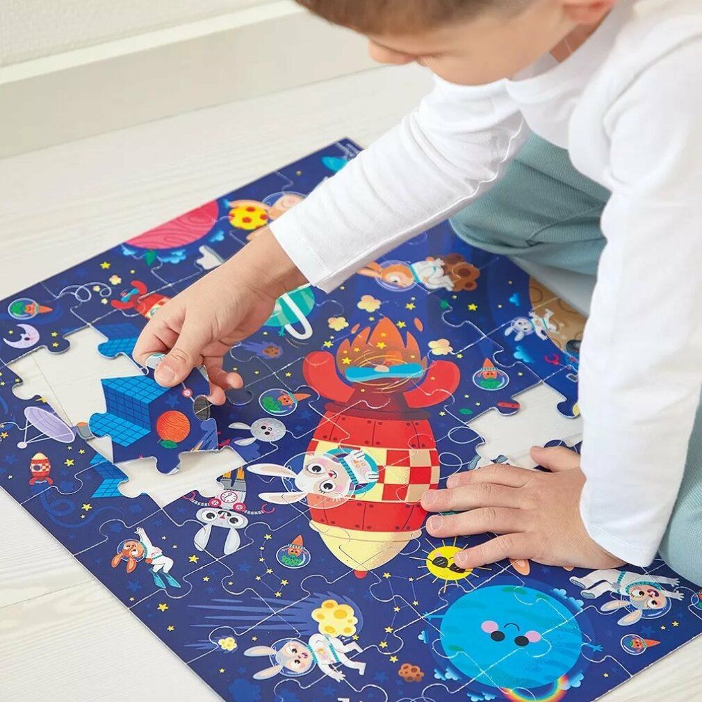 Bambino che mette un pezzo del puzzle. Puzzle Janod, 54 pezzi. Illustrazione di conigli in tuta spaziale, razzi, pianeti e stelle.