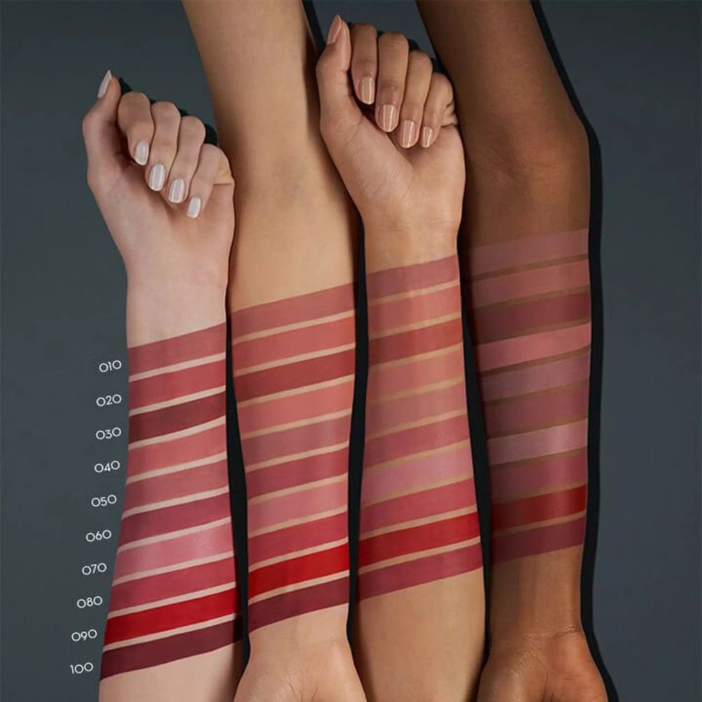 Braccia con campioni di rossetto in diverse tonalità di rosso. Diverse tonalità della pelle. Testo: 010 a 100.