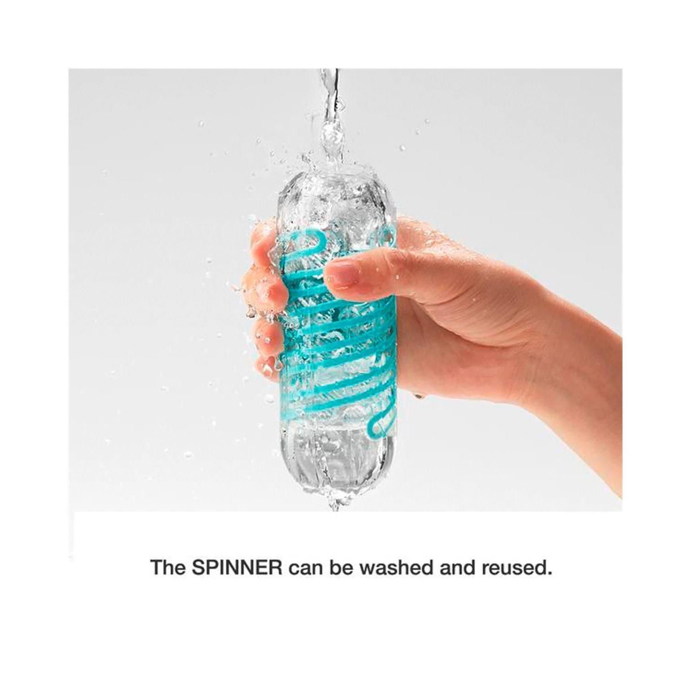 Mano che tiene un prodotto trasparente sotto l'acqua corrente. Spirale turchese visibile.