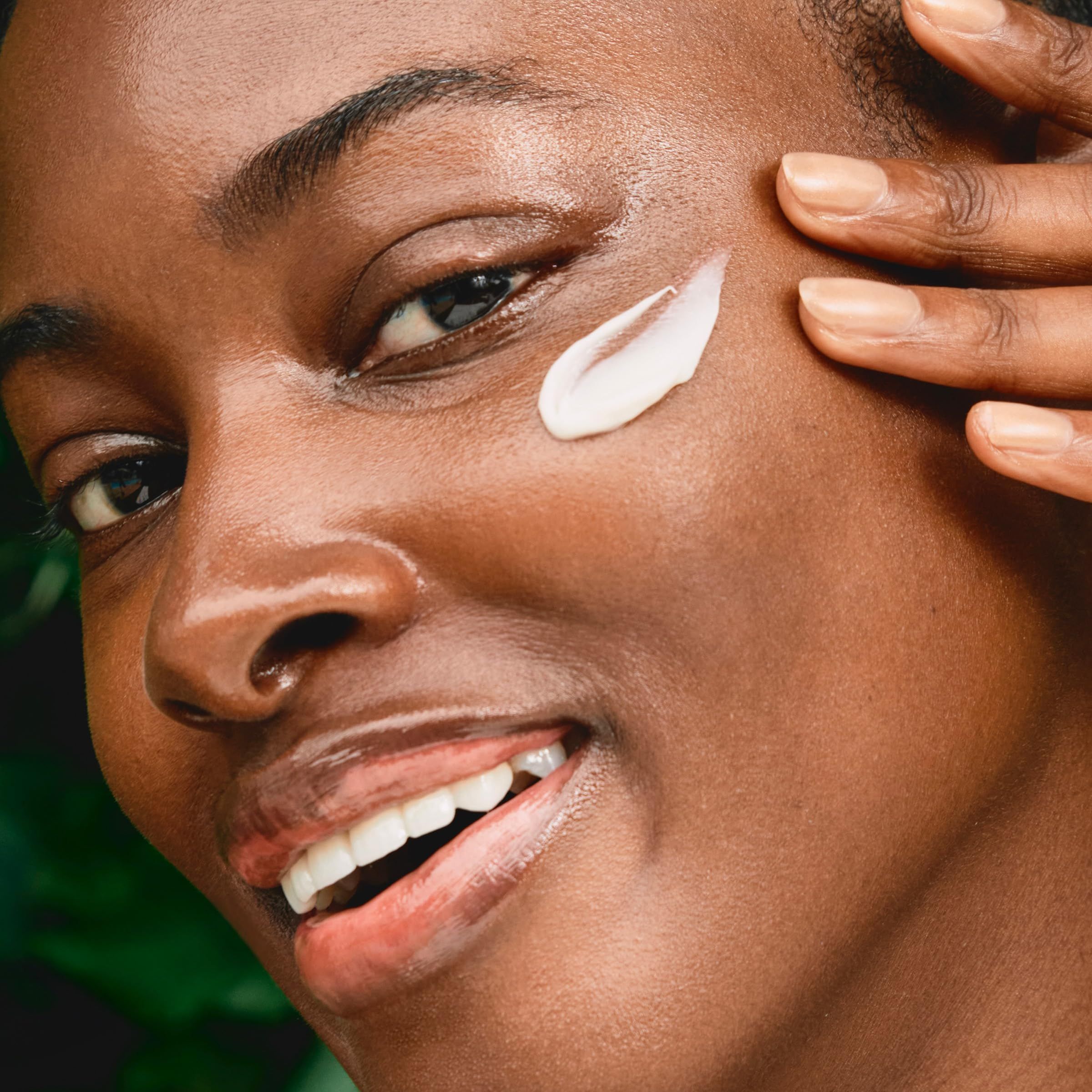 Donna applica crema sul viso. Crema sul dito. Espressione del viso: sorridente.