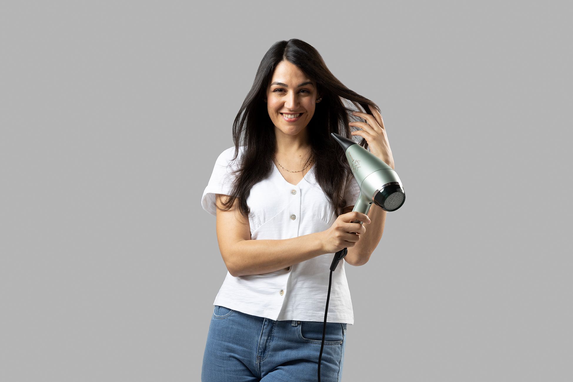 Una donna sorridente tiene in mano un asciugacapelli Remington argentato.