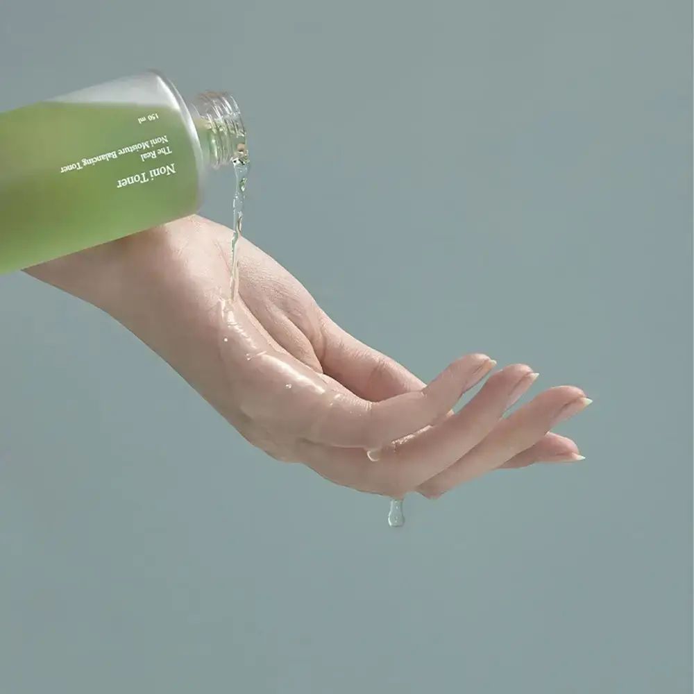 Toner verde versato da una bottiglia su una mano. Il toner è trasparente.