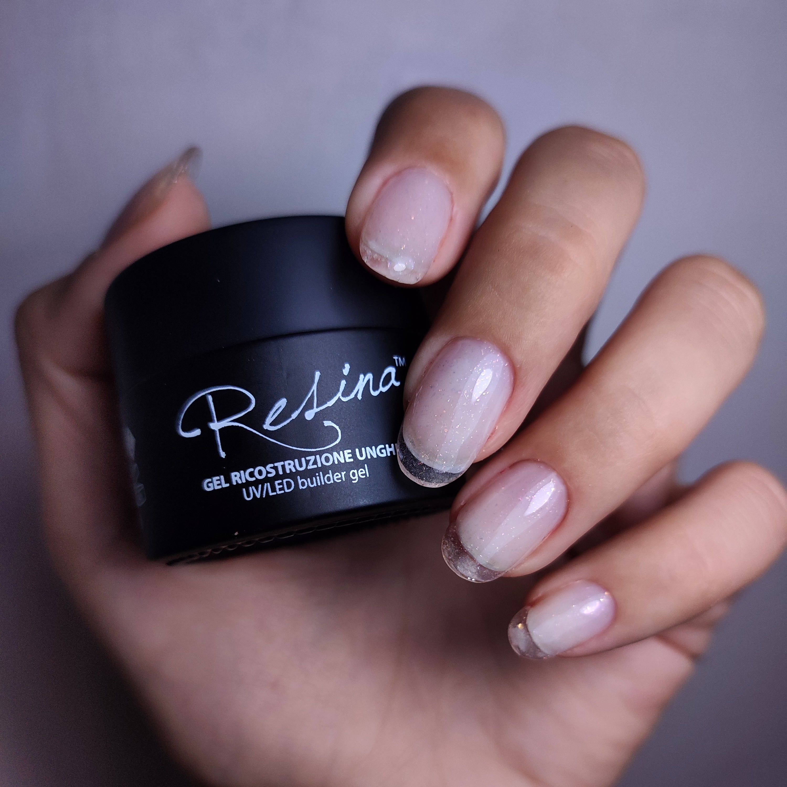 Vasetto nero con scritta bianca Resina e indicazione gel. Mano con unghie smaltate, french manicure con glitter.