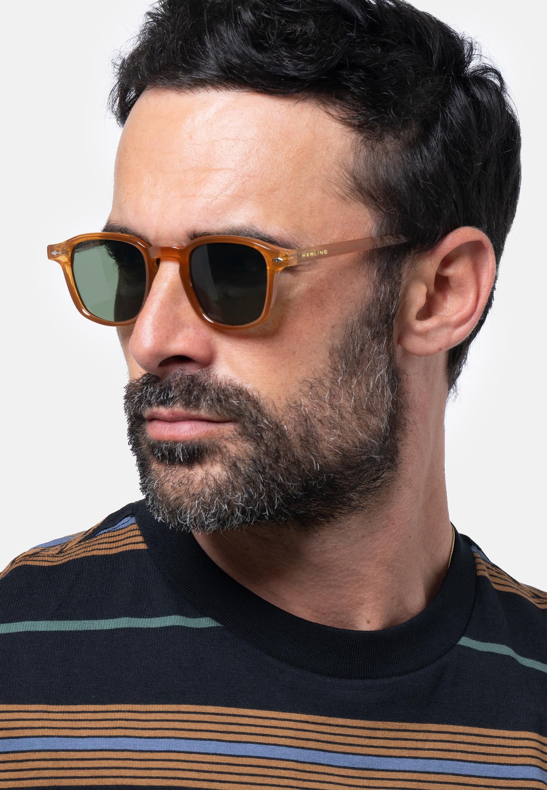 Uomo con occhiali da sole marroni e verdi. Logo Herling sull'asta.