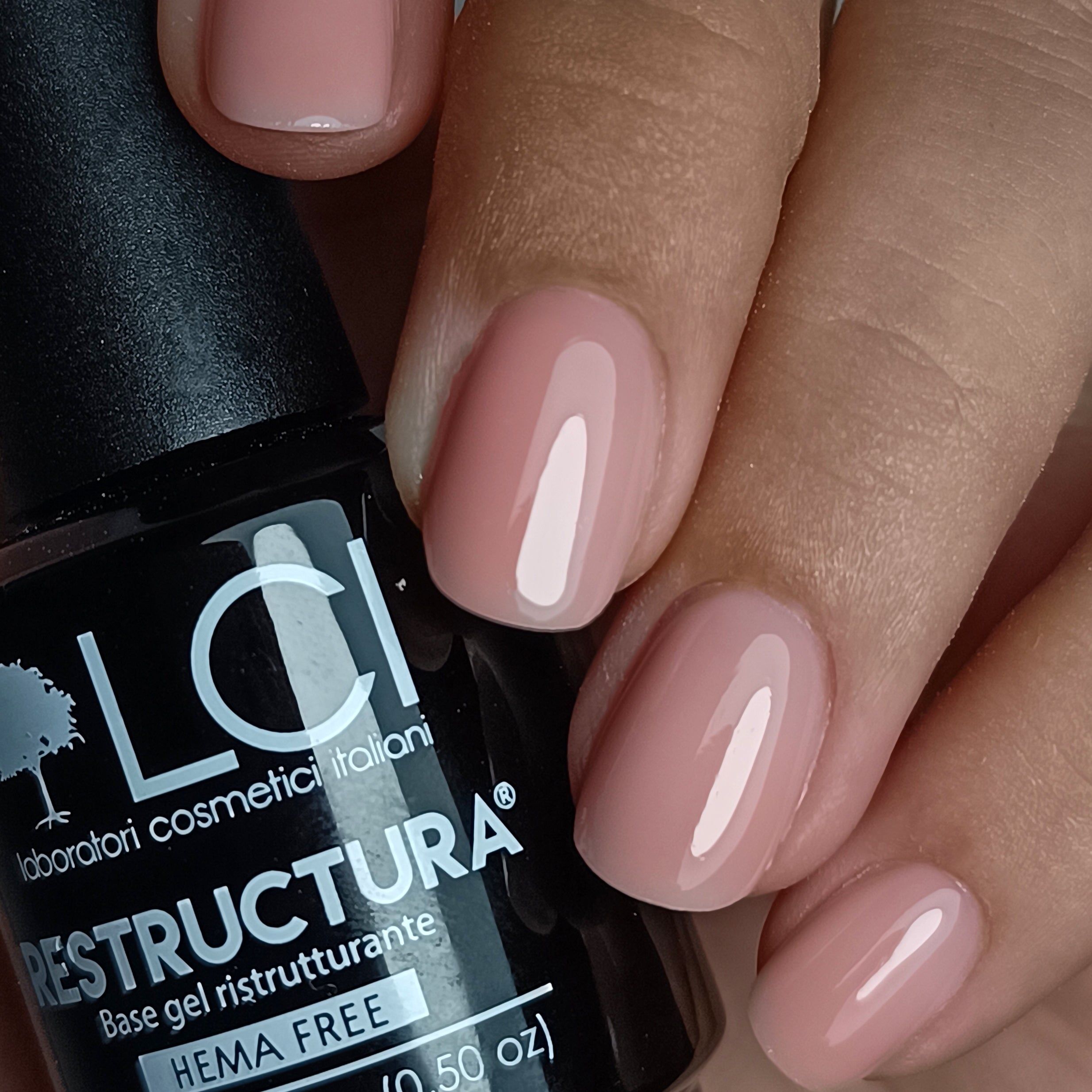 Flacone nero di smalto rosa accanto a unghie smaltate. Scritta: Restructura Base gel ristrutturante Hema Free.