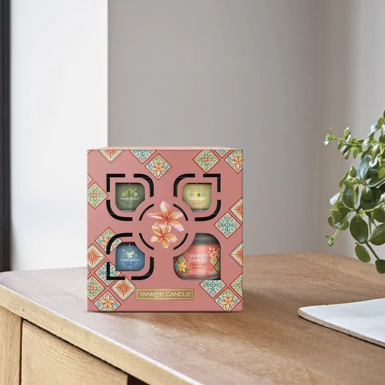 Confezione regalo Yankee Candle con quattro candele. Scatola rosa su tavolo in legno. Logo visibile.