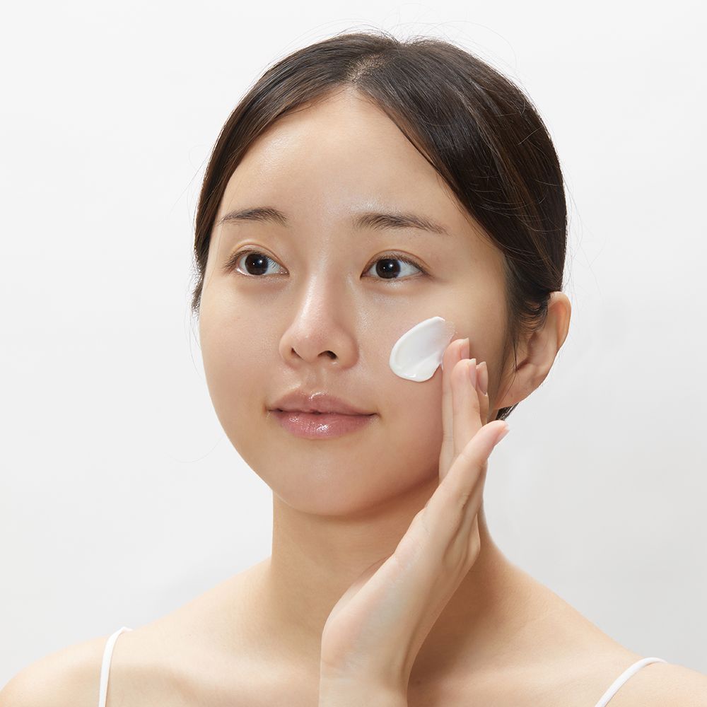 Una donna applica la crema sul viso. Ha i capelli scuri e indossa una canotta. Crema sul dito.