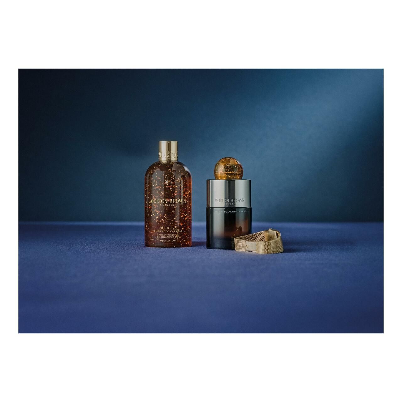 Tre prodotti su sfondo blu. Bottiglia, candela e coperchio. Liquido dorato e dettagli dorati.