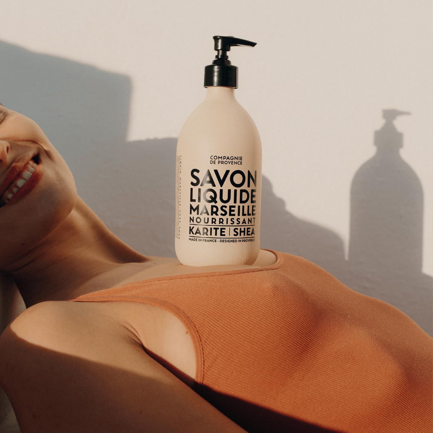 Flacone beige con erogatore nero su una persona. Testo: Savon Liquide Marseille Nourrissant Karité Shea.