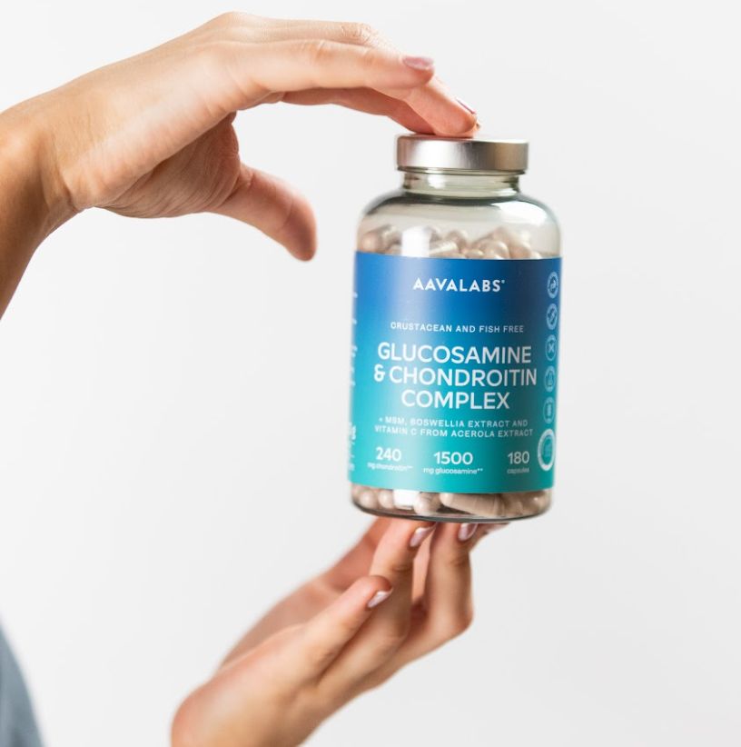 Mani che tengono una bottiglia di capsule di glucosamina.