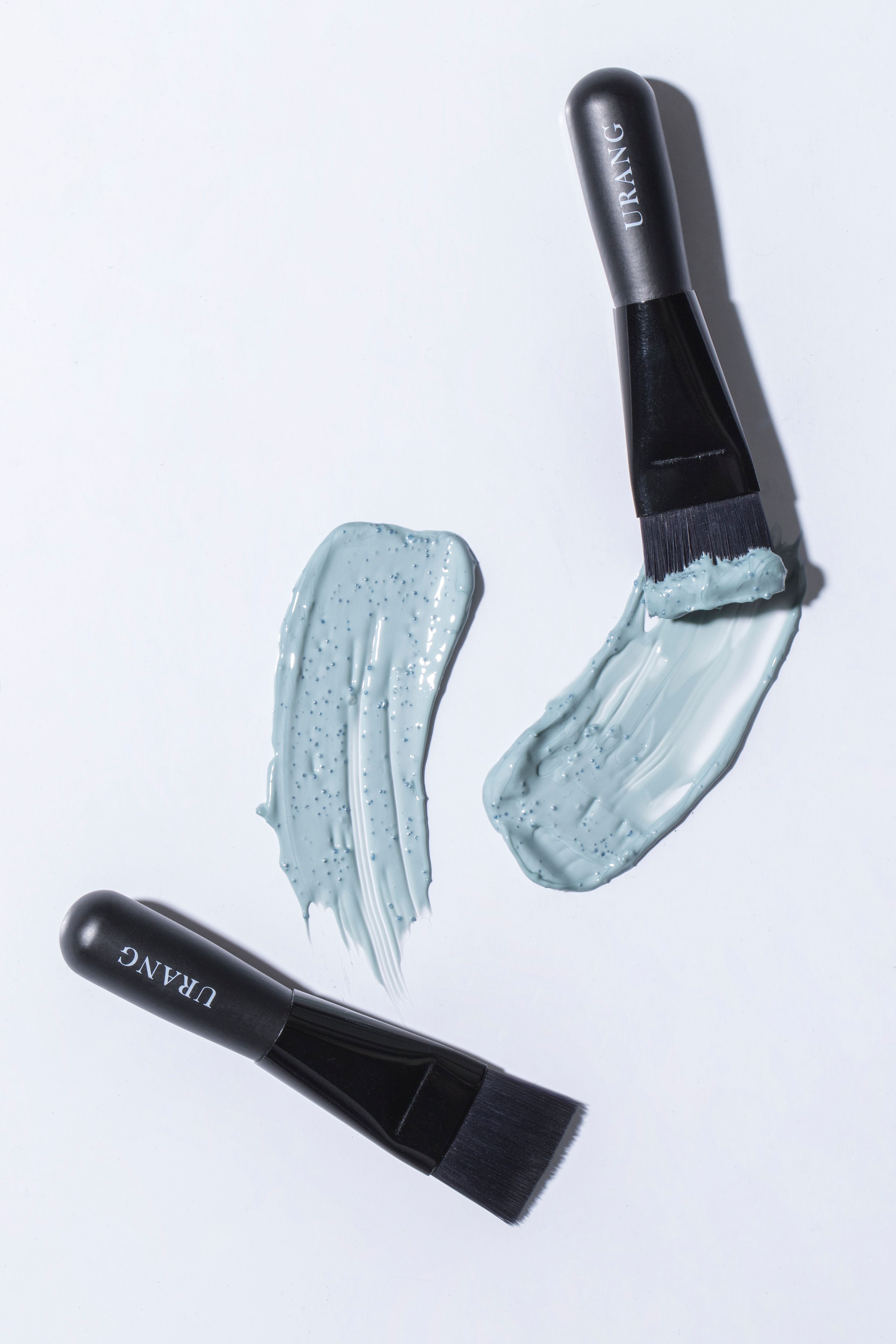 Tre pennelli neri con scritta URANG e tracce di crema blu. Pennelli con crema.