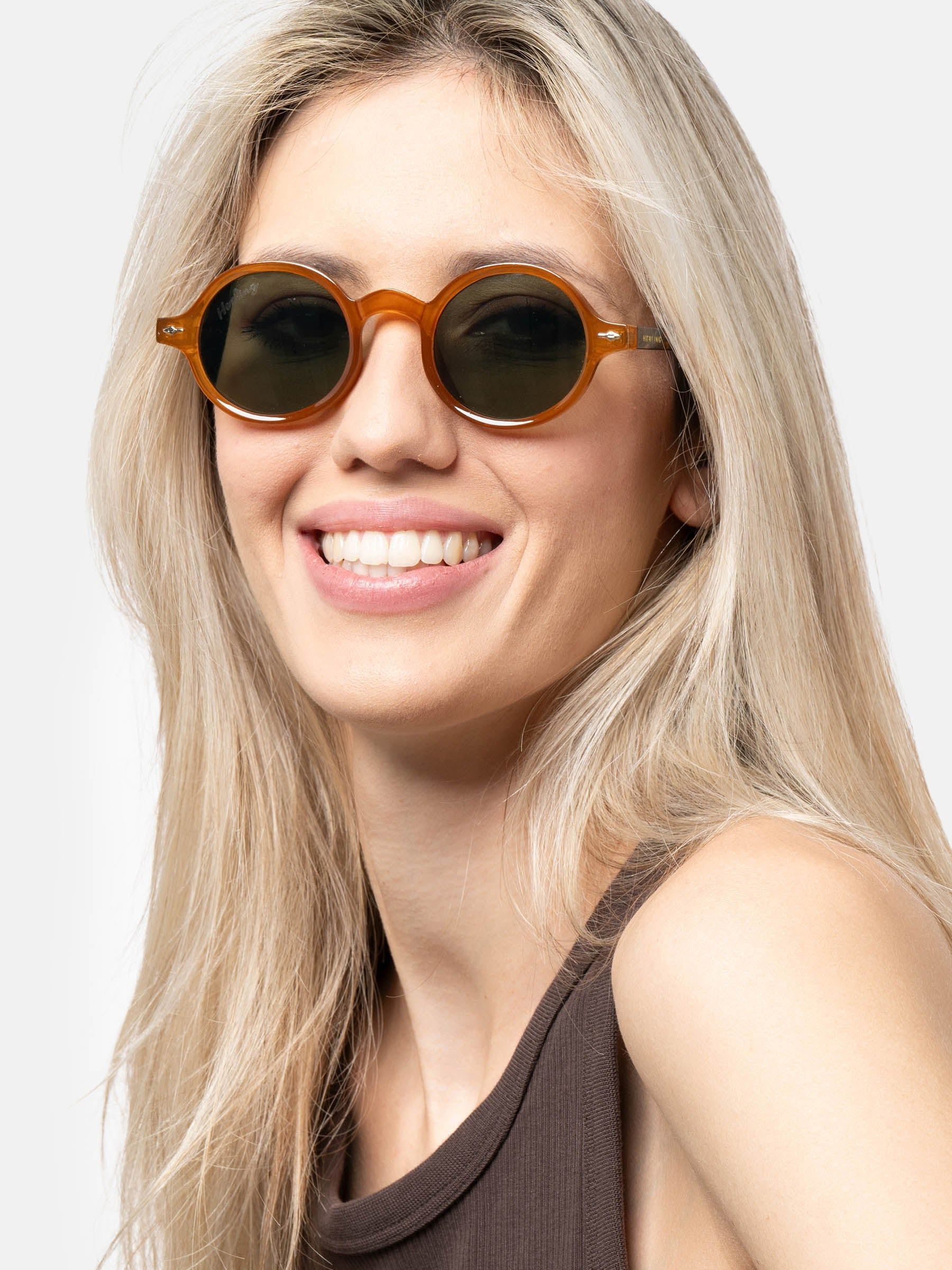 Donna bionda con occhiali da sole rotondi, montatura marrone, lenti verdi.