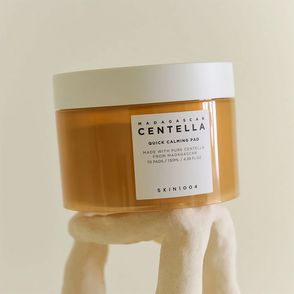 SKIN1004 Madagascar Centella Quick Calming Pad in un barattolo ambrato con coperchio bianco, su un piedistallo bianco.