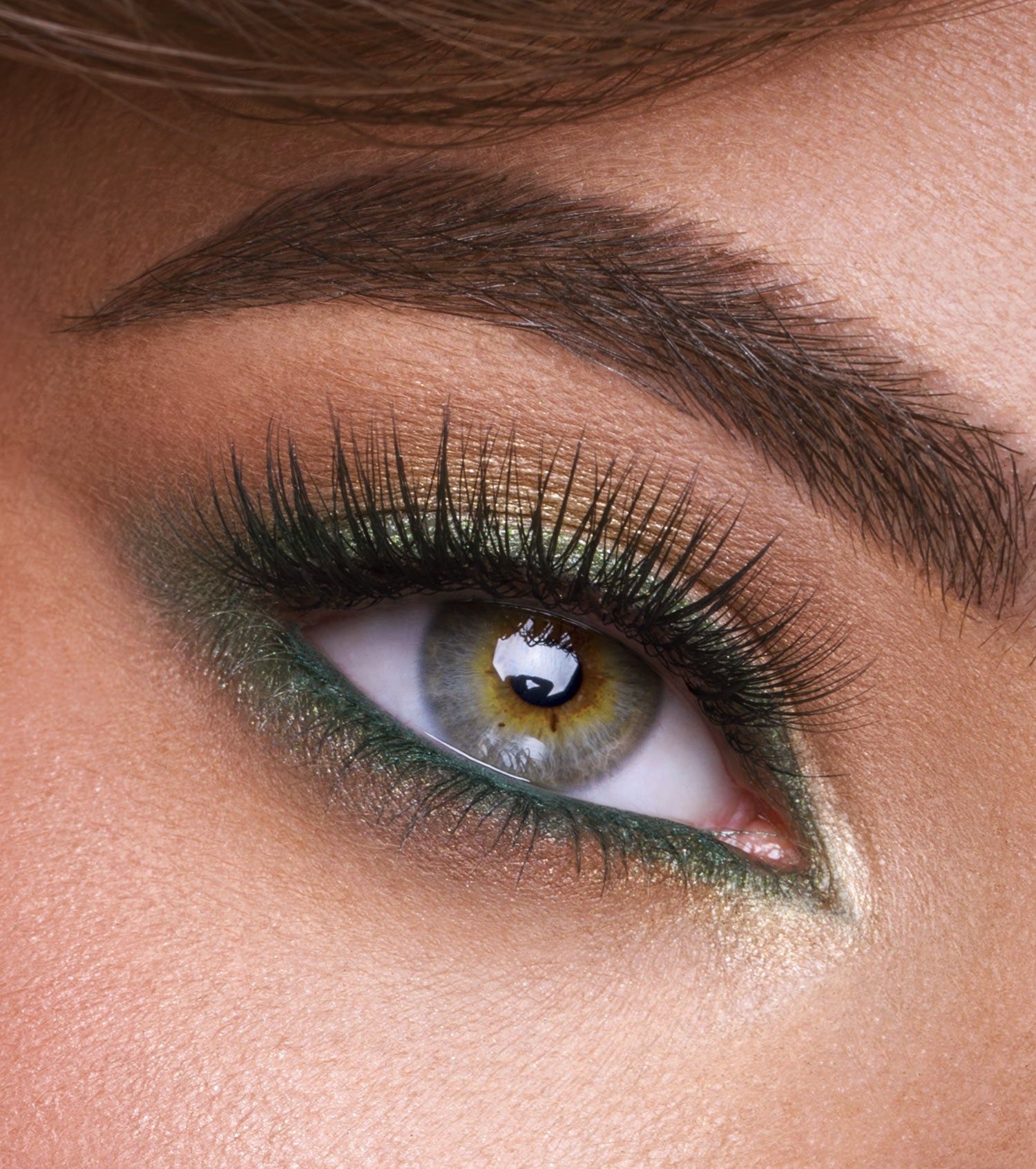 Primo piano di un occhio con ombretto verde e dorato, eyeliner e mascara.