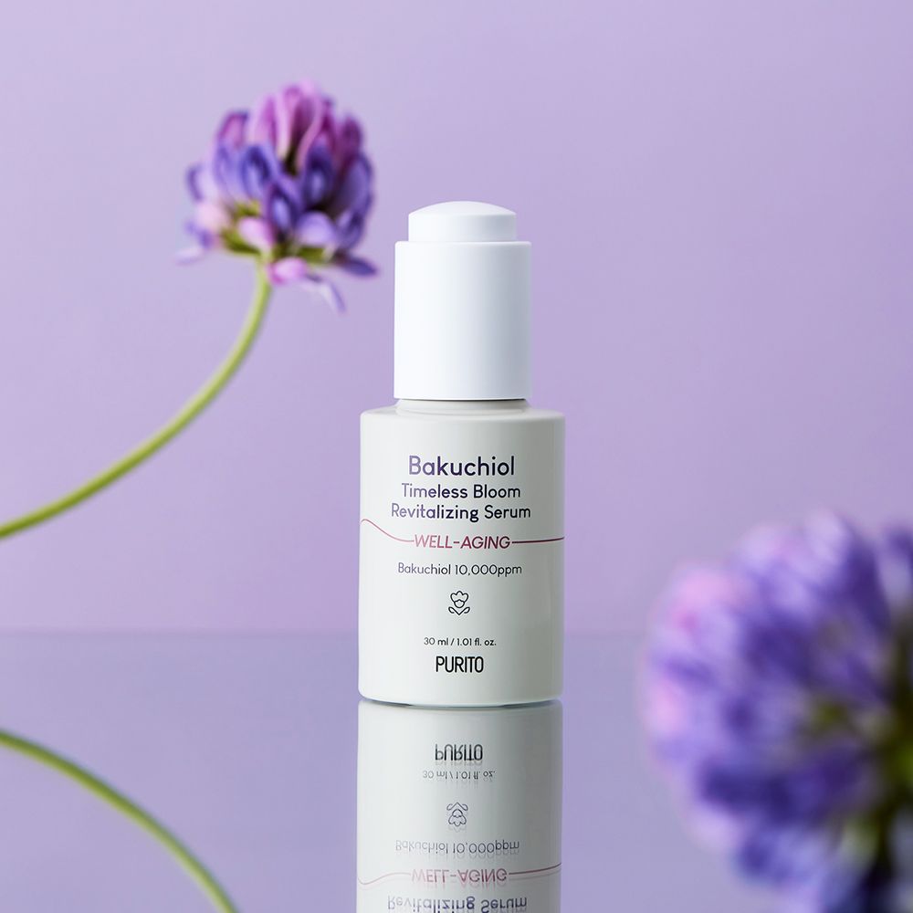 Flacone di siero bianco con scritta Bakuchiol Timeless Bloom. Con dosatore. Fiori viola sullo sfondo.