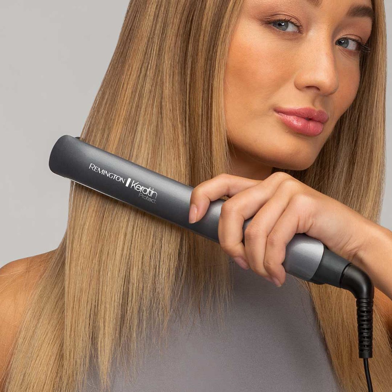 Donna liscia i capelli con una piastra grigia. Capelli biondi.