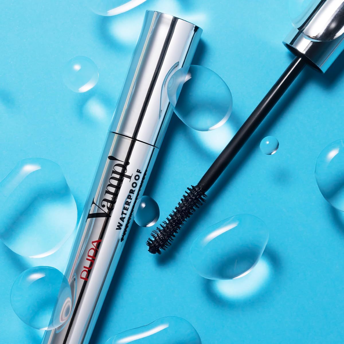 Tubo mascara con spazzola su sfondo blu con gocce d'acqua. Scritta: Vamp! Waterproof.