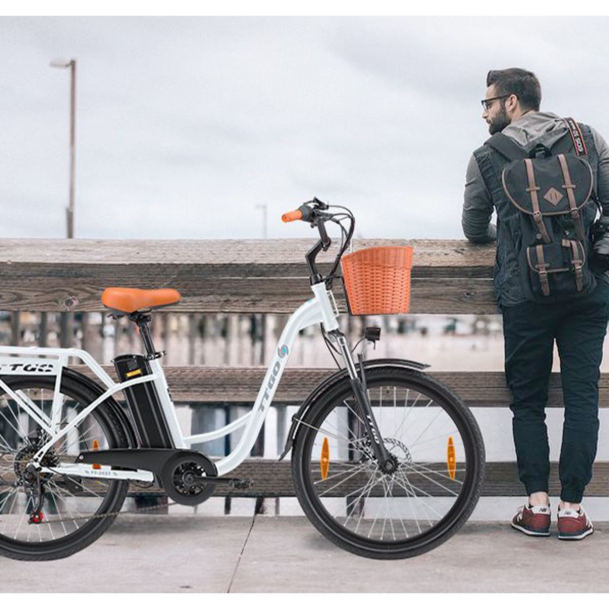 Persona in piedi accanto a bicicletta elettrica bianca con cestino. Sella e manopole marroni. Logo TTGO. Sfondo: pontile.