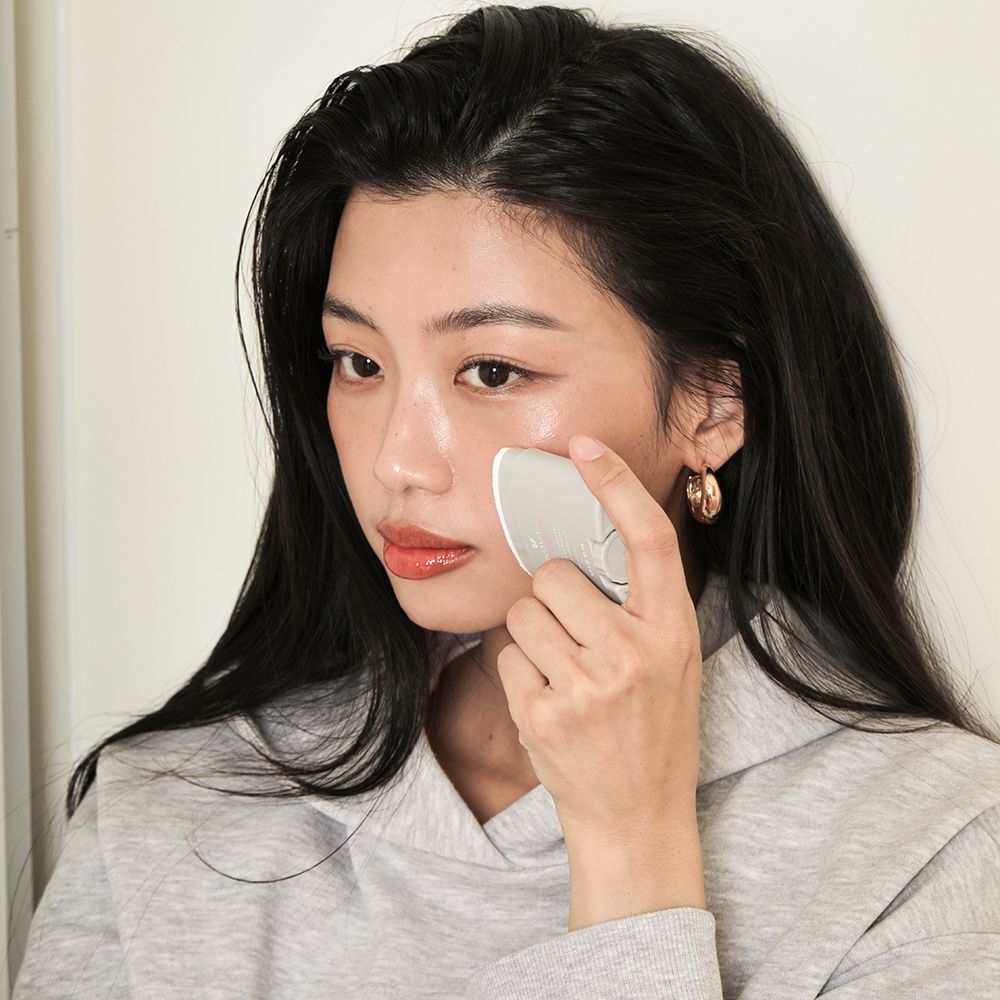 Donna con dispositivo per la cura della pelle. Dispositivo grigio, donna che tocca il viso. Sfondo bianco.