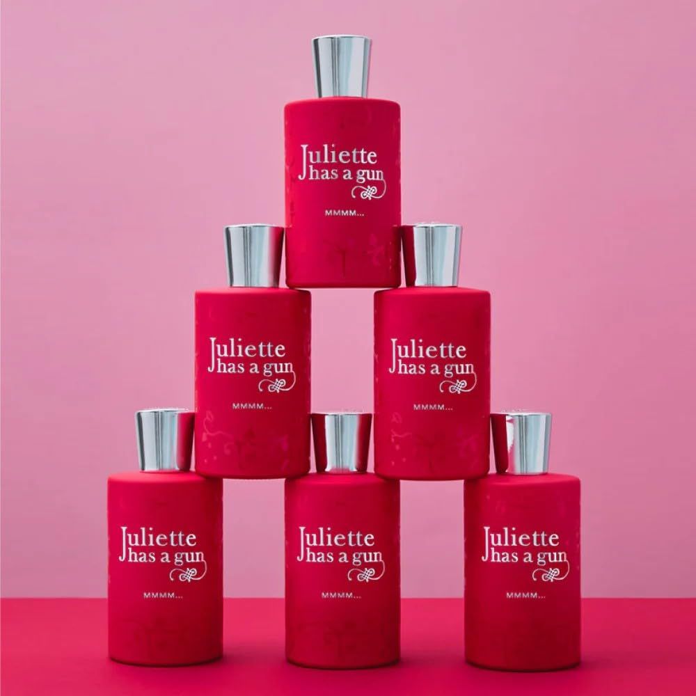 Sette flaconi di profumo rossi con tappi argentati. Scritta: Juliette has a gun. MMMM... Eau de Parfum. Su sfondo rosa.