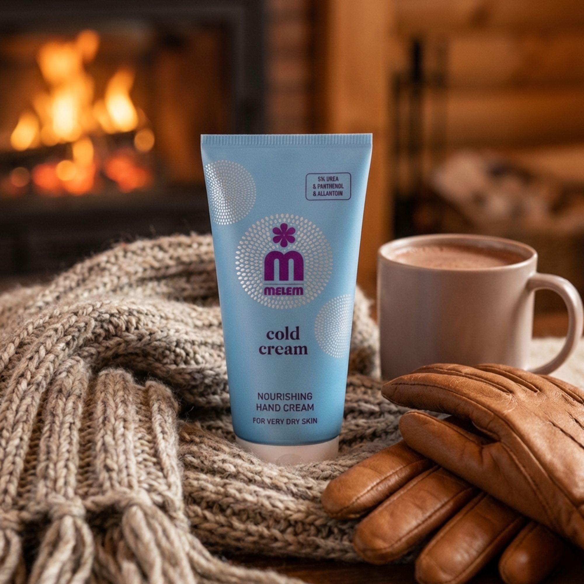 Tubo blu chiaro "Melem Cold Cream" su sciarpa di lana. Accanto, tazza e guanti in pelle. Camino sullo sfondo.